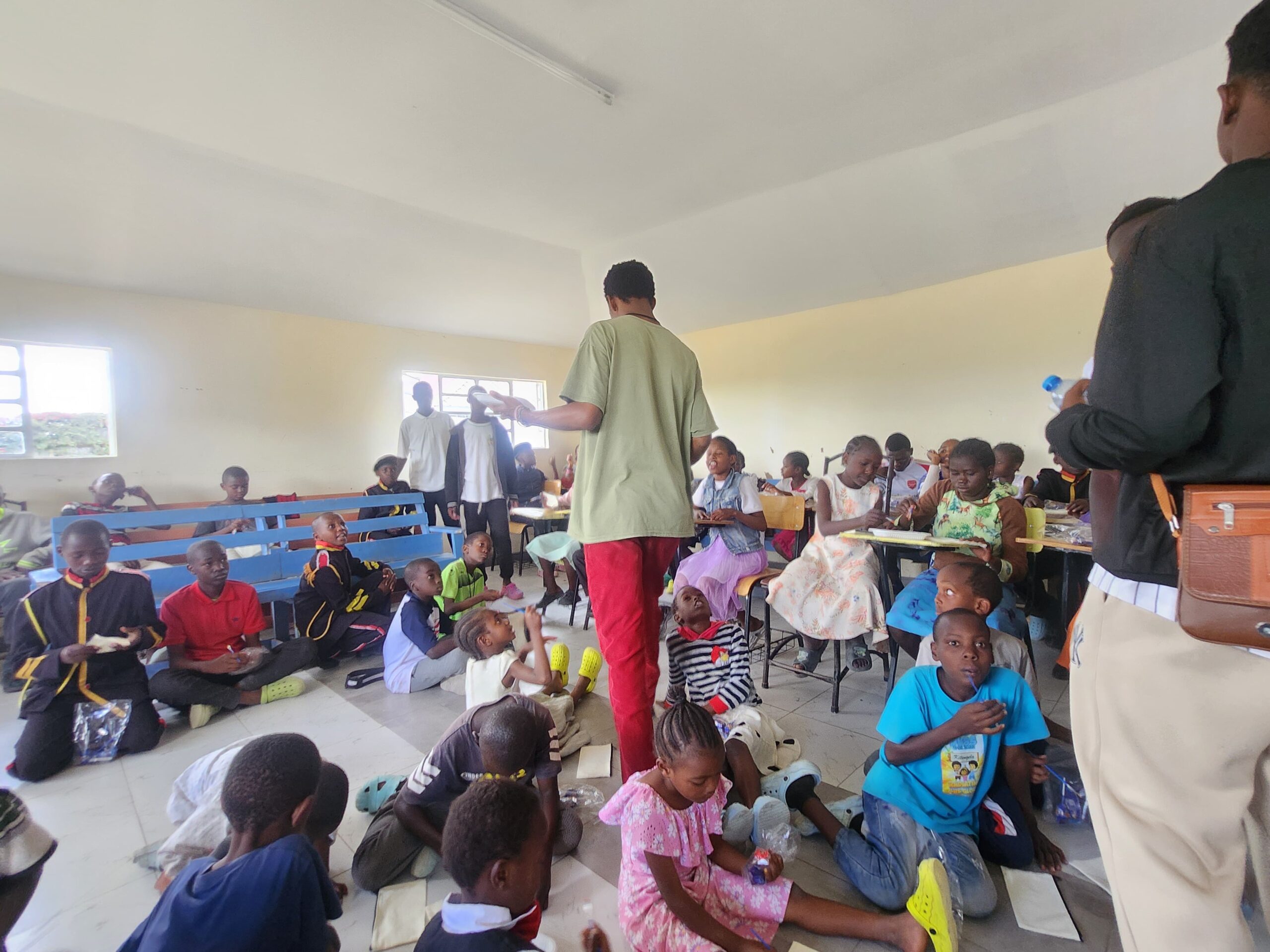 Children in class, some sited down, others sited on desks painting on small hand bags