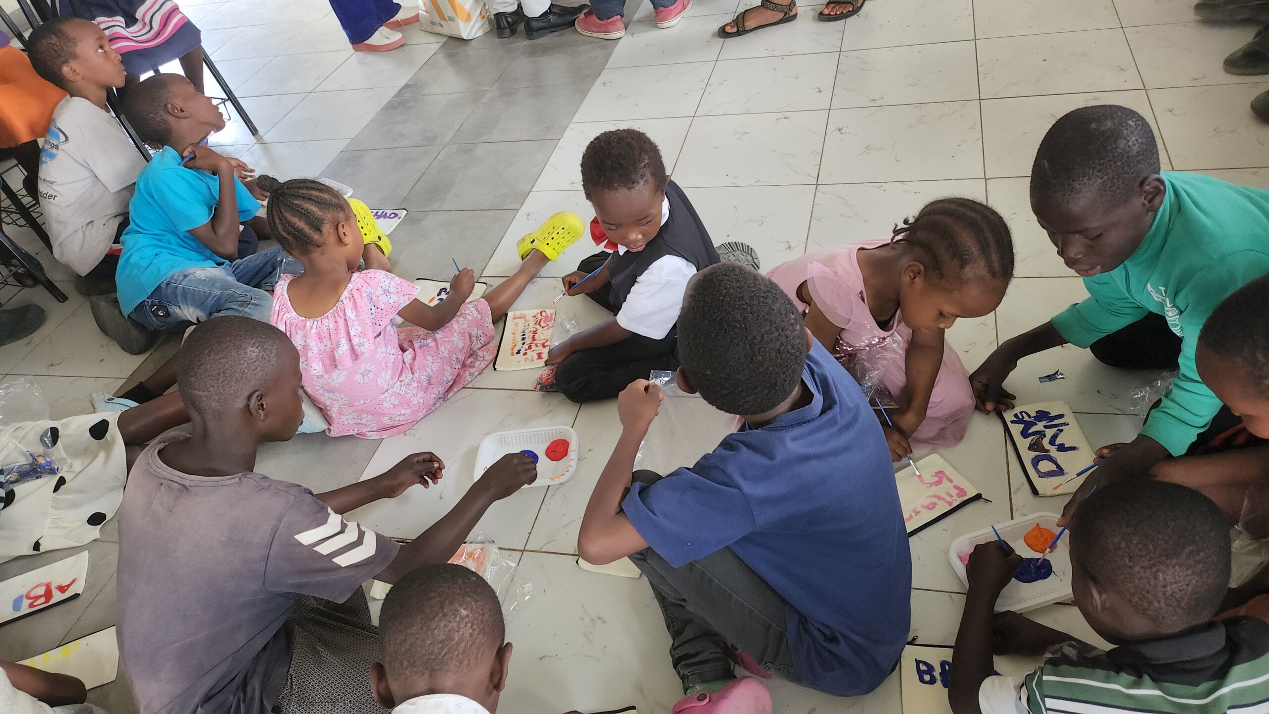 Children siting down in class painting on small hand bag